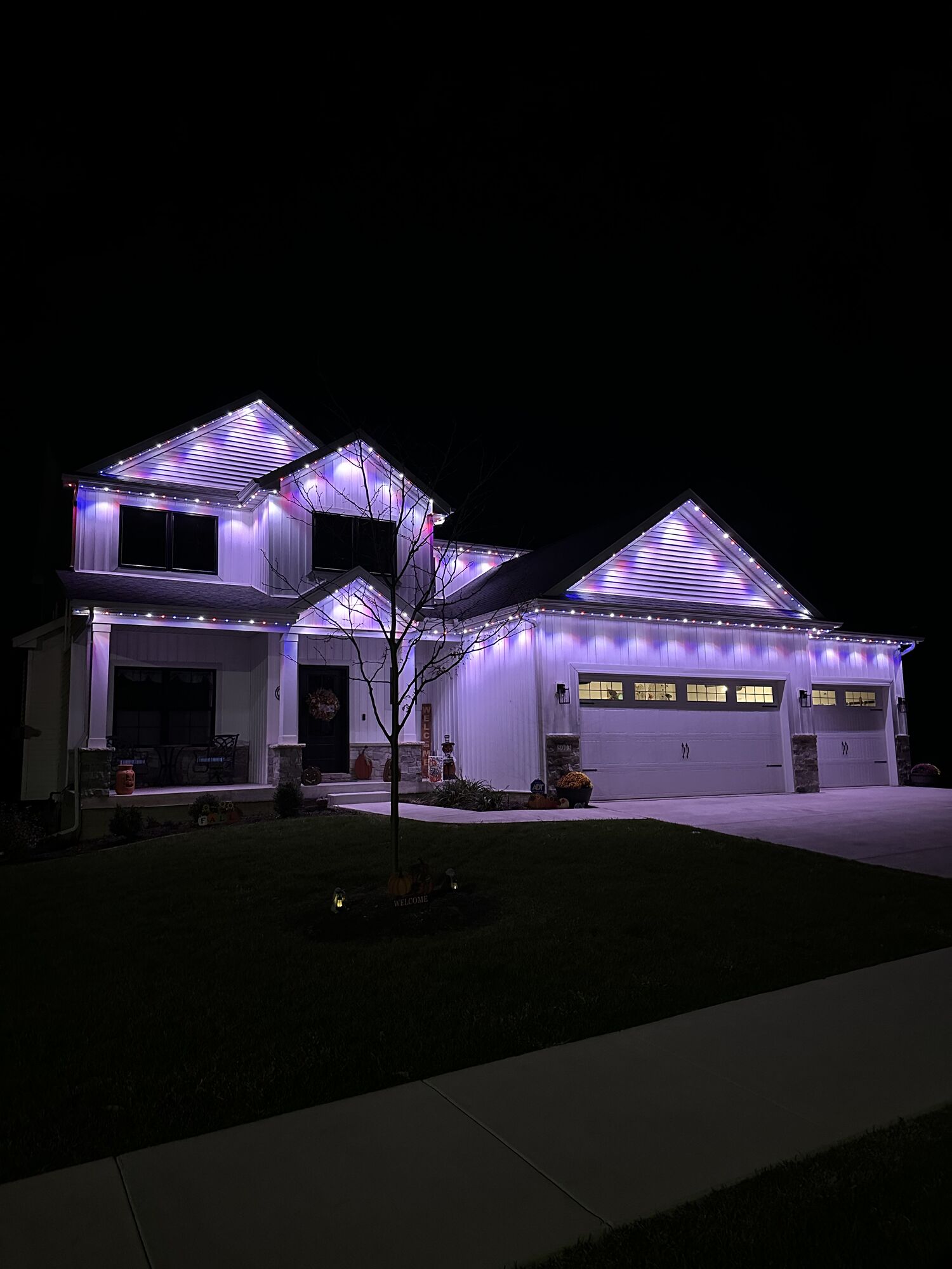 Two-story white home glowing in soft violet lighting along the eaves and gables